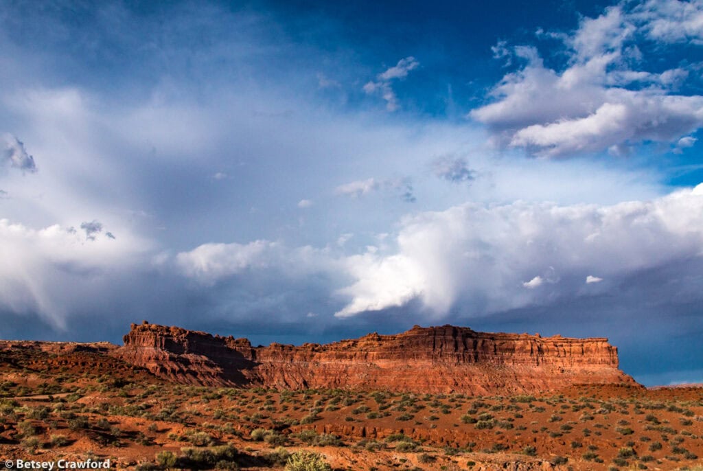 A red rock ridge in the Valley of the Gods in Utah under dramatic clouds in a very blue sky. Photo by Betsey Crawford