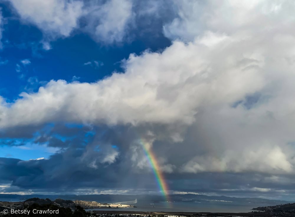 A rainbow arches down from dramatic clouds over San Francisco Bay. Photo by Betsey Crawford.